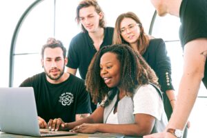Un groupe diversifié de jeunes professionnels collaborant autour d'un ordinateur portable dans un environnement de bureau moderne. Idéal pour les concepts commerciaux ou technologiques.