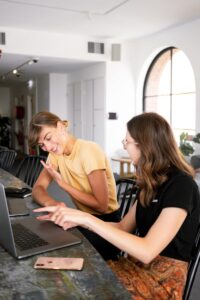 Deux femmes engagées dans une discussion collaborative dans un bureau moderne autour d'ordinateurs portables.