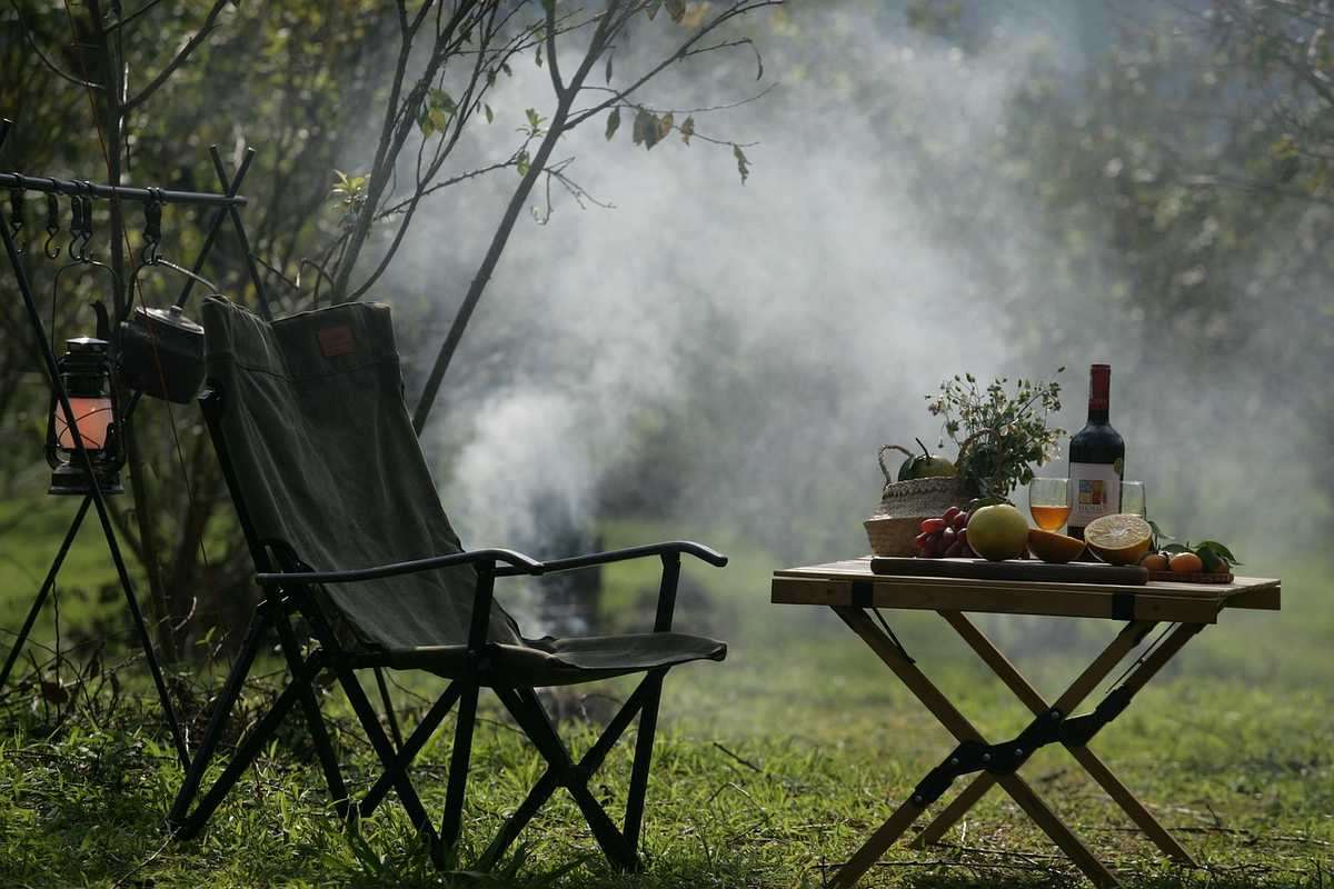 Chaise et table de camping avec fruits, vin et provisions face à un paysage brumeux