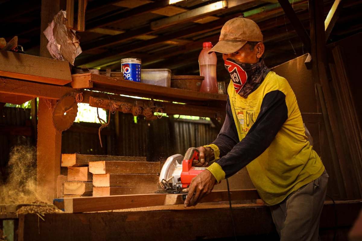 Homme en jaune et noir coupe bois avec scie dans atelier en bois