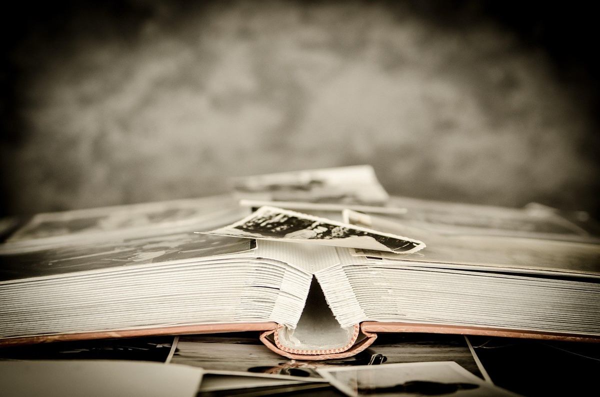 Livre ouvert avec pages blanches et photos éparpillées sur une table Livre ouvert avec pages blanches et photos éparpillées sur une table