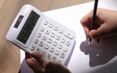 Une main utilise une calculatrice tandis que l'autre écrit sur un papier blanc