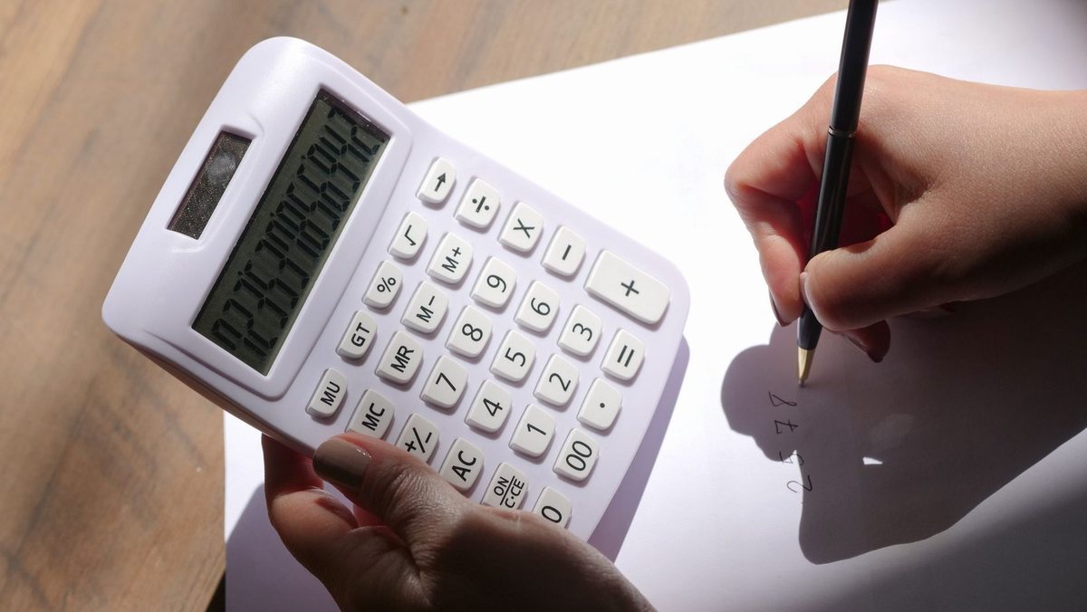 Une main utilise une calculatrice tandis que l'autre écrit sur un papier blanc