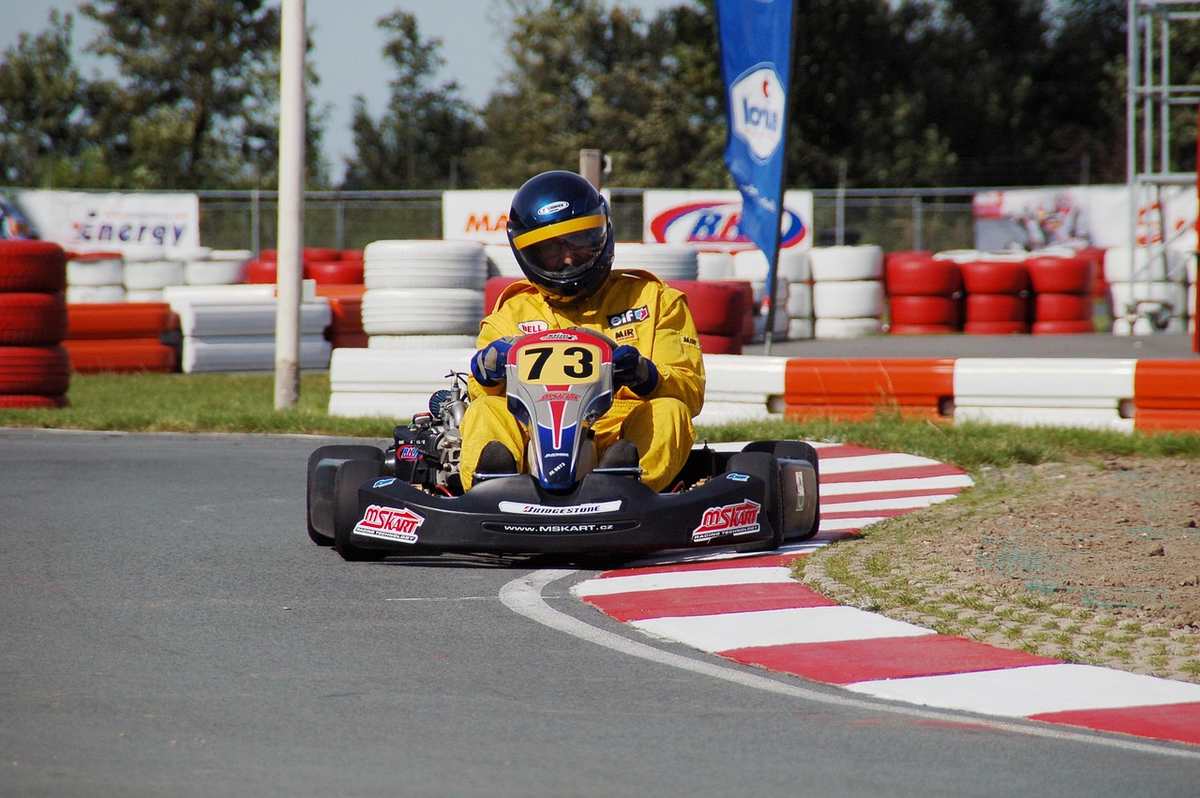 Un coureur en kart jaune number 73 tourne un virage sur piste