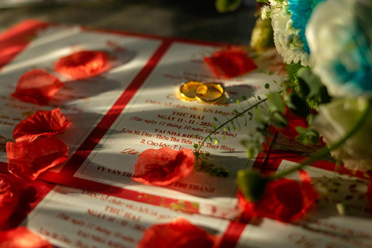 Cartes d'invitation, alliances d'or, pétales de rose et fleurs sous lumière