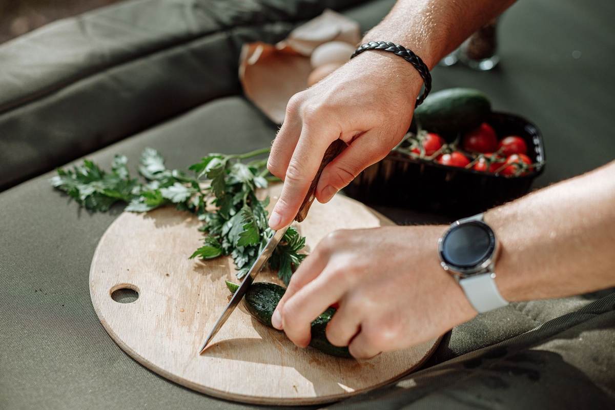 Mains coupant un légume sur une planche en bois, assiette de tomates et œufs à proximité Mains coupant un légume sur une planche en bois, assiette de tomates et œufs à proximité