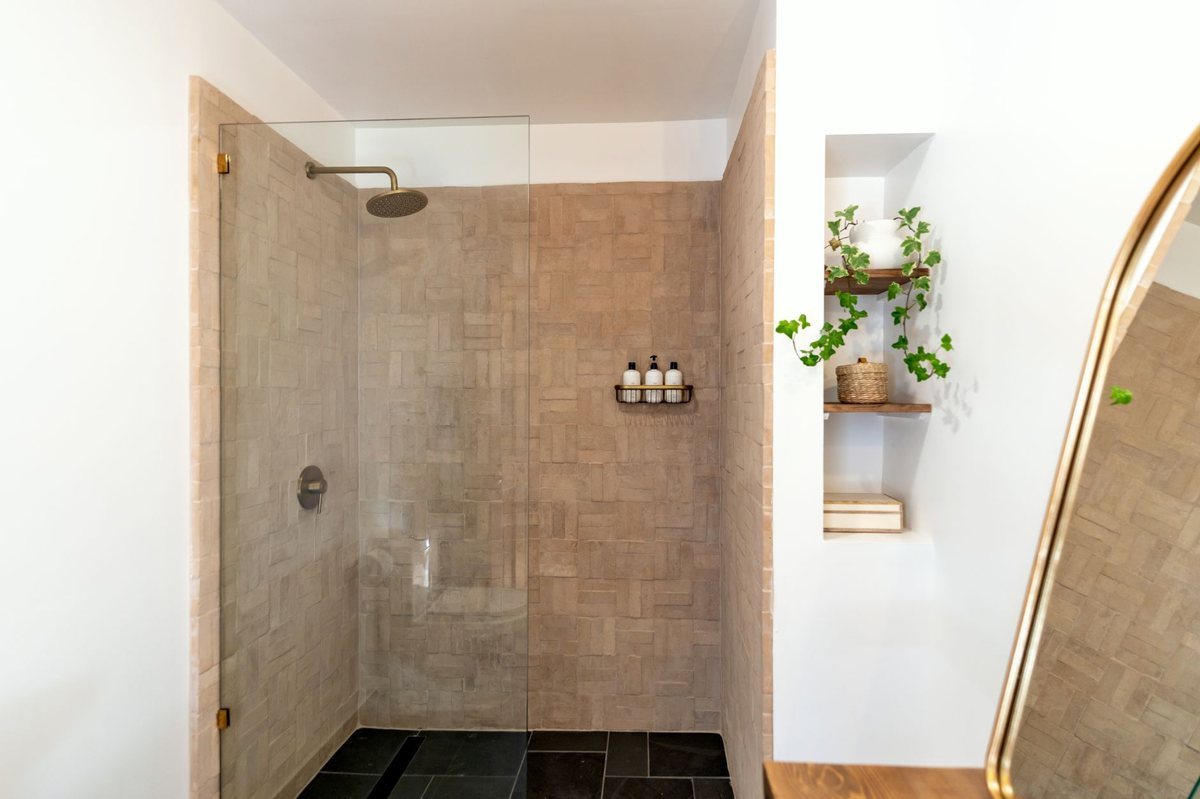 Douche à l'italienne avec verre, carrelage beige, étagère et plantes