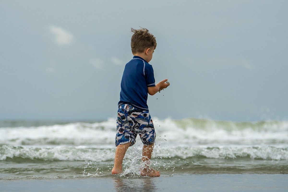 Enfant dans l'eau de mer, marée haute, ciel nuageux Enfant dans l'eau de mer, marée haute, ciel nuageux