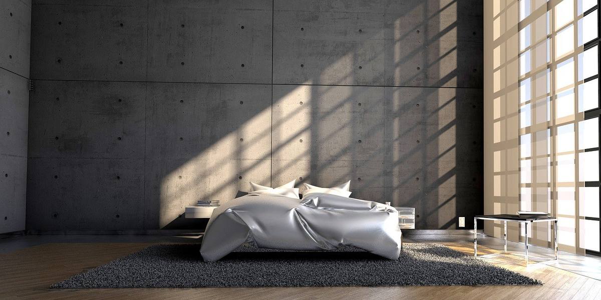 Chambre avec lit queen size drap argenté, coussins blancs, parquet, tapis gris, mur en béton, lumière naturelle Chambre avec lit queen size drap argenté, coussins blancs, parquet, tapis gris, mur en béton, lumière naturelle