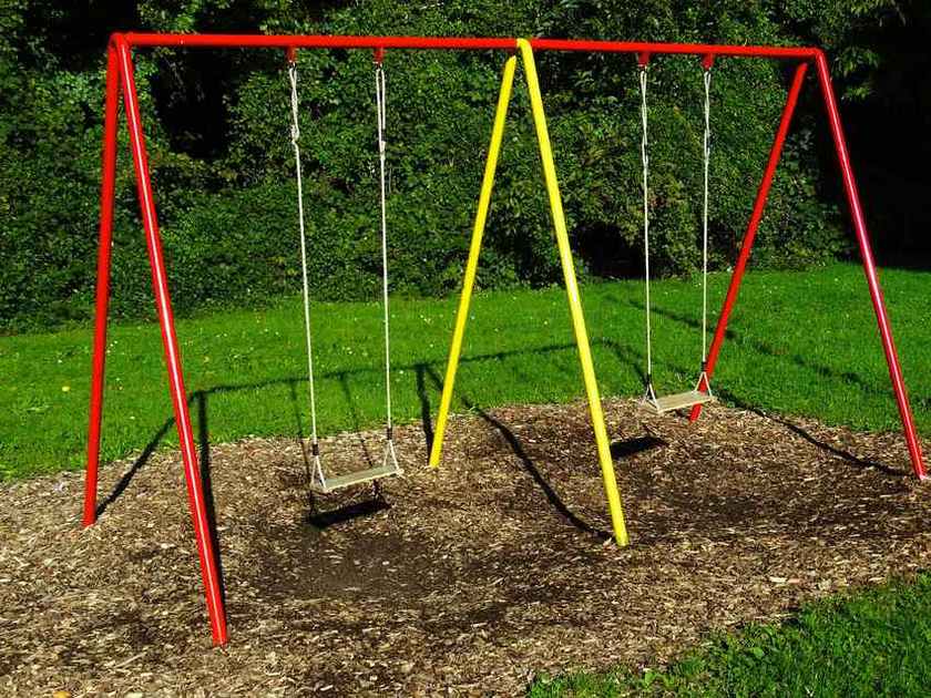 Portique de balançoires rouge et jaune sur sol de copeaux dans jardin vert Portique de balançoires rouge et jaune sur sol de copeaux dans jardin vert